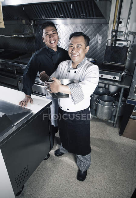 Deux cuisiniers masculins posant dans la cuisine du restaurant commercial . — Photo de stock