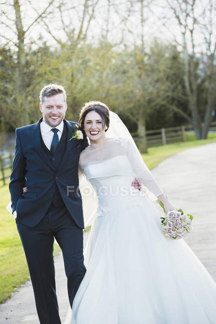 Braut und Bräutigam posieren im Sonnenlicht auf dem Weg und lachen. — Stockfoto