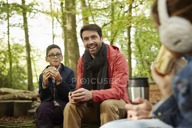 Padre e hijos bebiendo té en el bosque en otoño . - foto de stock