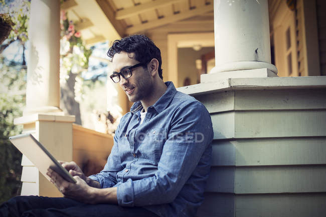 Человек с цифровым планшетом на крыльце в загородном доме . — стоковое фото