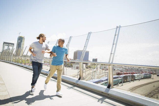 Two young men jogging along city bridge. — Stock Photo