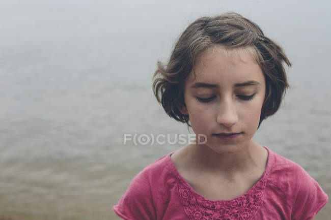 Portrait of moody pre-adolescent girl in front of lake water. — Stock Photo
