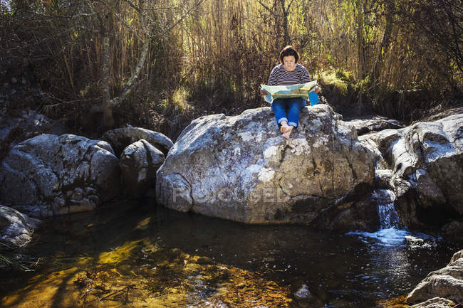 Mujer sentada en las rocas junto al río y mirando el mapa
. - foto de stock