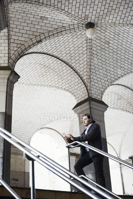 Metà uomo adulto in piedi sulle scale sotto l'arco e guardando il telefono cellulare . — Foto stock