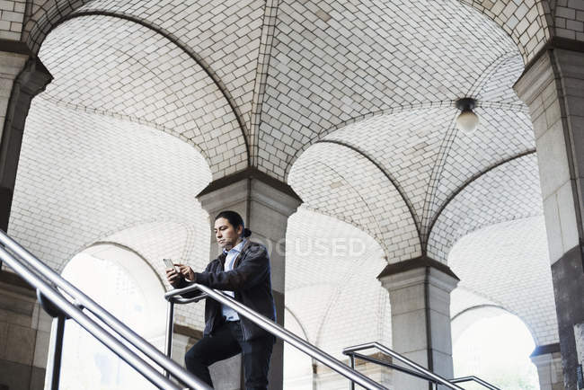 Hombre adulto de pie en las escaleras bajo el arco y mirando el teléfono móvil . - foto de stock