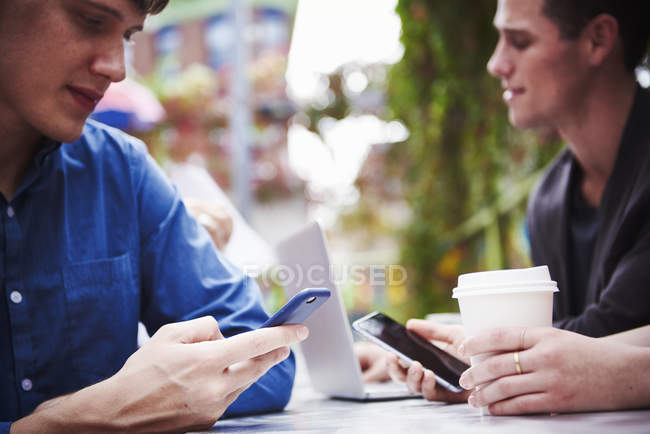 Young men sitting at table in city and working with laptop computer and phones. — Stock Photo