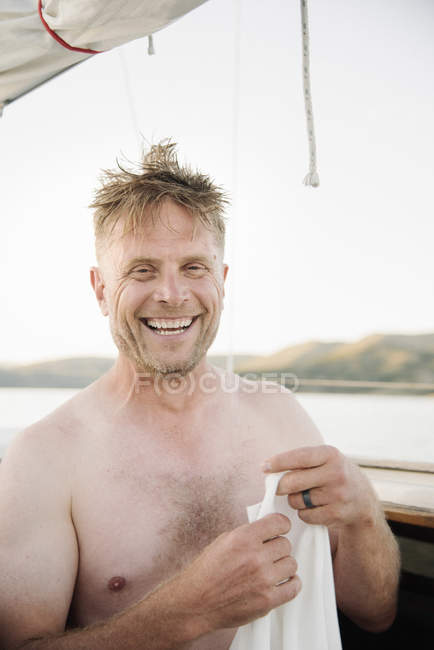 Sonriente hombre sin camisa de pie en velero con camiseta en las manos . - foto de stock