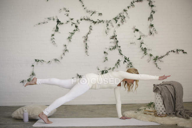 Woman on yoga white mat with leg raised and arm outstretched. — Stock Photo