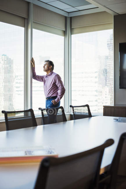 Mature man in meeting room leaning and looking through window. — Stock Photo