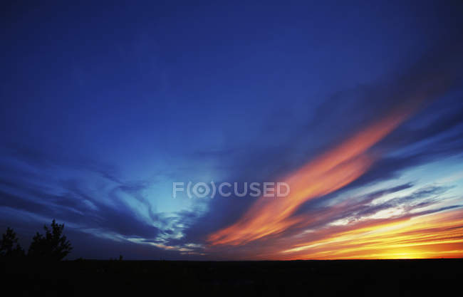 Wellen des Sonnenlichts von untergehender Sonne, die Wolken am abdunkelnden Himmel erhellen. — Stockfoto