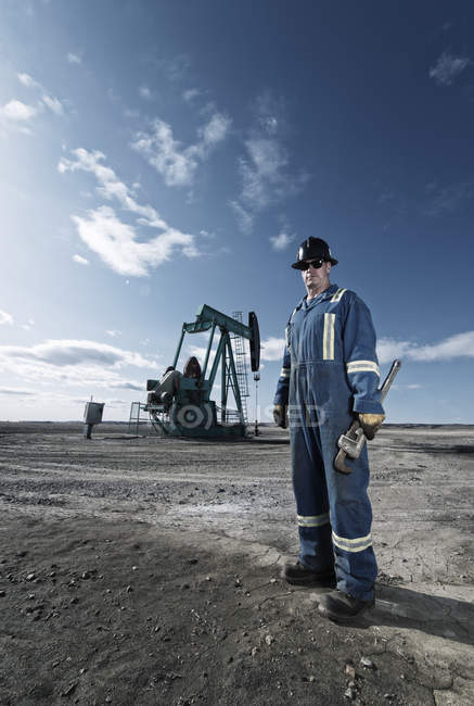 Homme en salopette et casque au cric de la pompe en pleine terre sur le site d'extraction d'huile . — Photo de stock