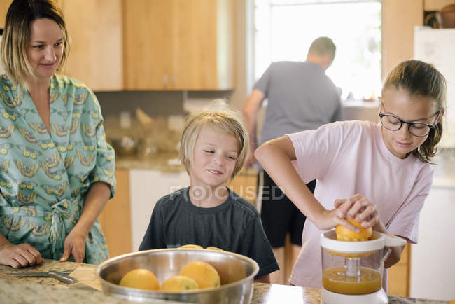 Mädchen quetscht mit Familie Orangen und bereitet Frühstück in Küche zu. — Stockfoto