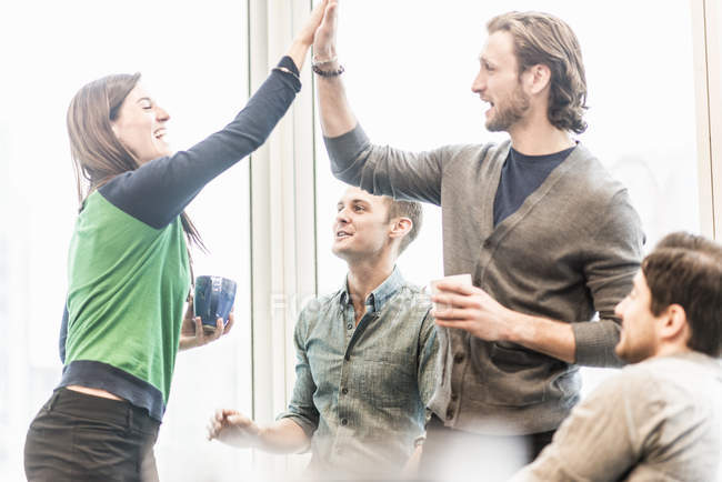 Colleagues laughing and sharing high five gesture on coffee break. — Stock Photo