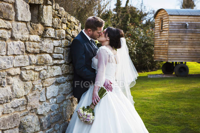 Жених и невеста целуются в день свадьбы, стоя в саду . — стоковое фото