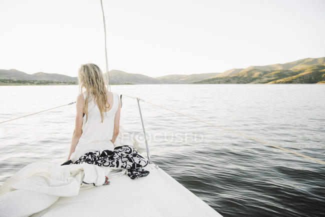 Blonde teenage girl sitting on sailboat bow at lake. — Stock Photo