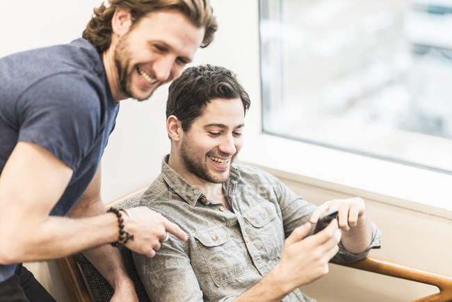 Homem verificando smartphone com colega no escritório . — Fotografia de Stock