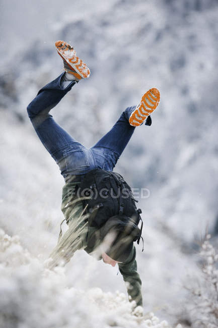 Wanderer mit Rucksack macht Handstand auf schneebedecktem Hang. — Stockfoto