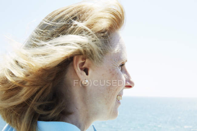 Perfil de blonde mature woman standing by ocean . - foto de stock