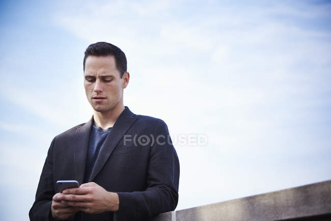 Молодой человек стоит на крыше и смотрит вниз на смартфон . — стоковое фото