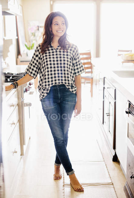 Mulher com longos cabelos castanhos em pé na cozinha e sorrindo . — Fotografia de Stock