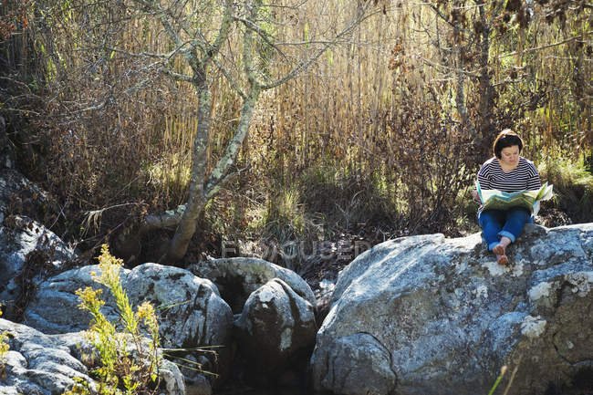 Woman sitting on rocks by river and looking at map. — Stock Photo