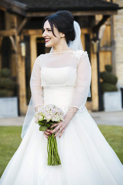 Braut im Brautkleid trägt Blumenstrauß im Freien. — Stockfoto