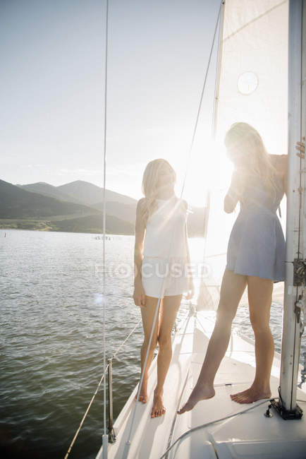 Zwei Teenager-Mädchen stehen im Gegenlicht auf Segelboot am See. — Stockfoto