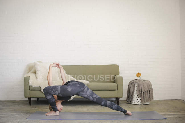 Mulher loira dobrando no tapete de ioga com pernas separadas e braços levantados . — Fotografia de Stock