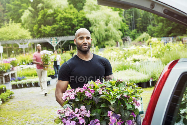 Man loading flowers into trunk of car parked at garden center. — Stock Photo