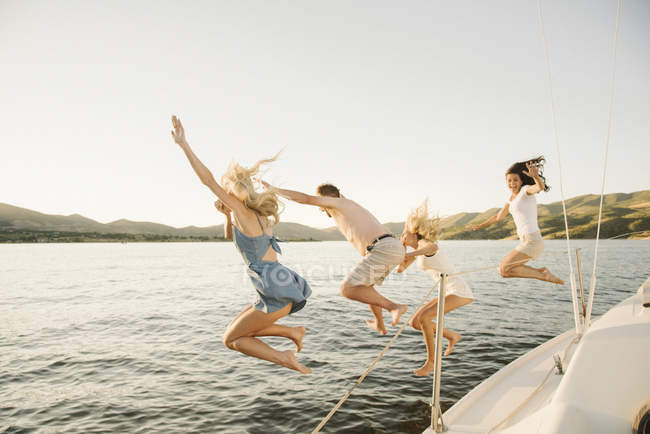 Батьки з доньками-підлітками стрибають з вітрильника в озерну воду . — стокове фото