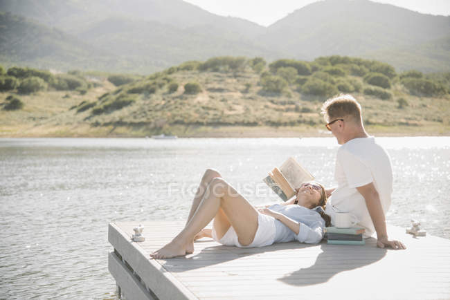 Man and woman reclining on jetty and reading book. — Stock Photo