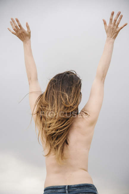 Rückansicht einer oben ohne stehenden Frau mit erhobenen Armen unter bewölktem Himmel. — Stockfoto