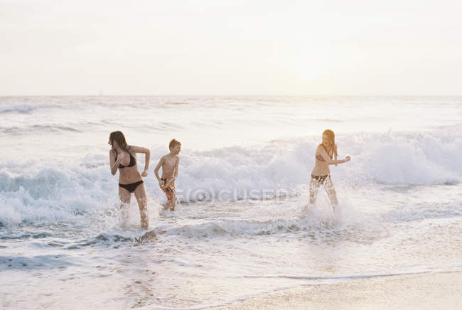 Teenage girls and pre-teen boy playing on sandy beach by ocean. — Stock Photo