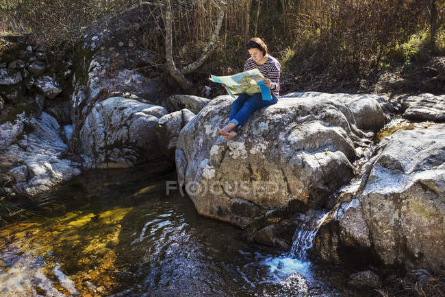 Mulher sentada em rochas junto ao rio e olhando para o mapa . — Fotografia de Stock