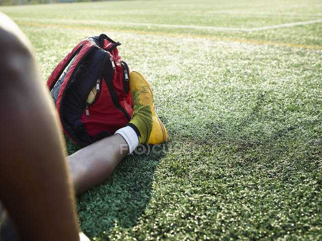 Мужские ноги в желтой спортивной обуви на зеленой лужайке с рюкзаком на ногах . — стоковое фото