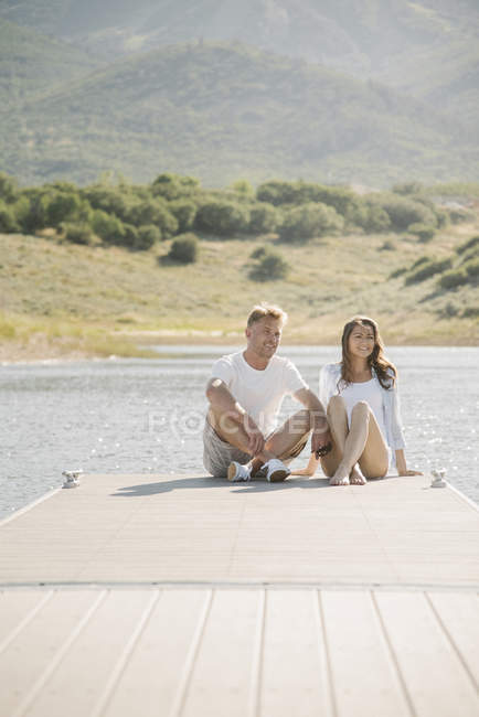 Uomo e donna seduti fianco a fianco sul molo, vista frontale . — Foto stock