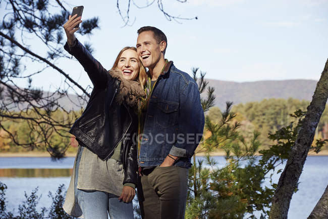 Hombre y mujer tomando selfie en la orilla del lago en otoño . - foto de stock