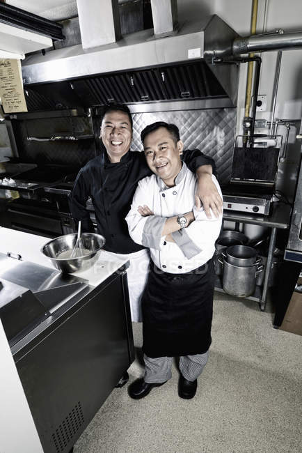 Deux cuisiniers masculins posant dans la cuisine du restaurant commercial . — Photo de stock