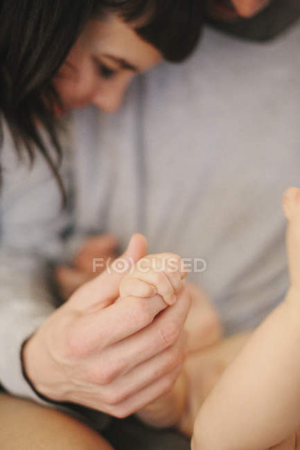 Close-up of male hand clasping baby resting in parents arms. — Stock Photo