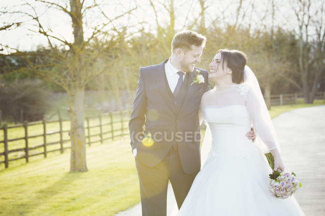 Bride and groom walking down path in soft light outdoors. — Stock Photo
