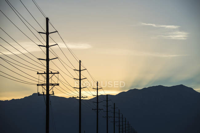 Fila de postes e linhas de comunicação ao pôr do sol na paisagem montanhosa . — Fotografia de Stock