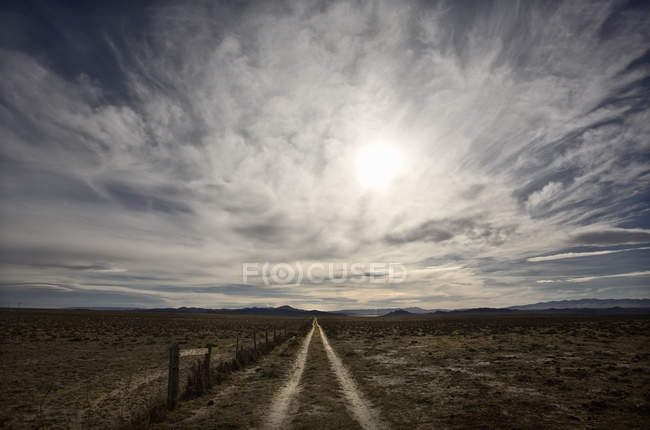 Céu com nuvens sobre a pradaria e estrada de terra levando à distância . — Fotografia de Stock