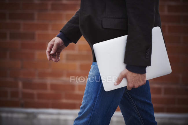 Ausgeschnittene Ansicht eines Mannes, der mit Laptop auf der Straße läuft. — Stockfoto