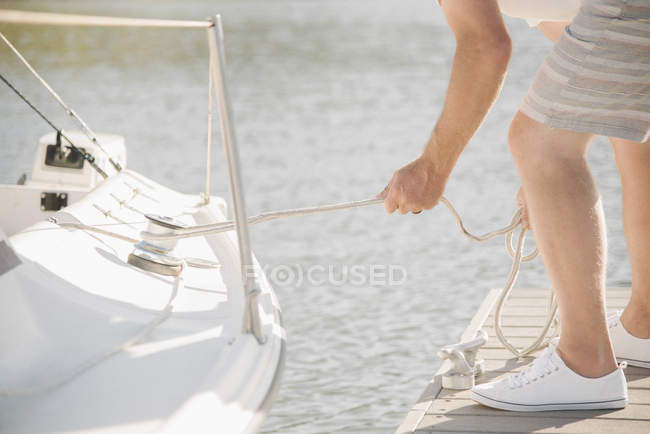 Uomo in piedi sul molo e rimorchio barca a vela con corda . — Foto stock