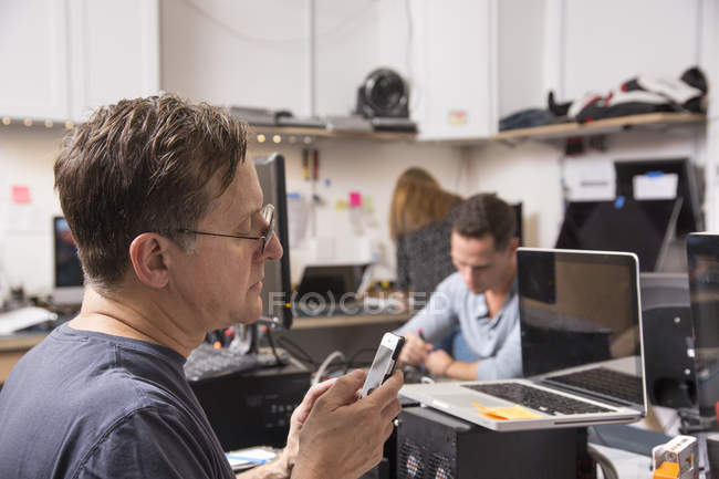 Зрелый мужчина смотрит на телефон в техническом салоне лаборатории . — стоковое фото