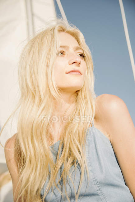 Junge blonde Frau unter Segeln auf Boot vor blauem Himmel, Portrait. — Stockfoto