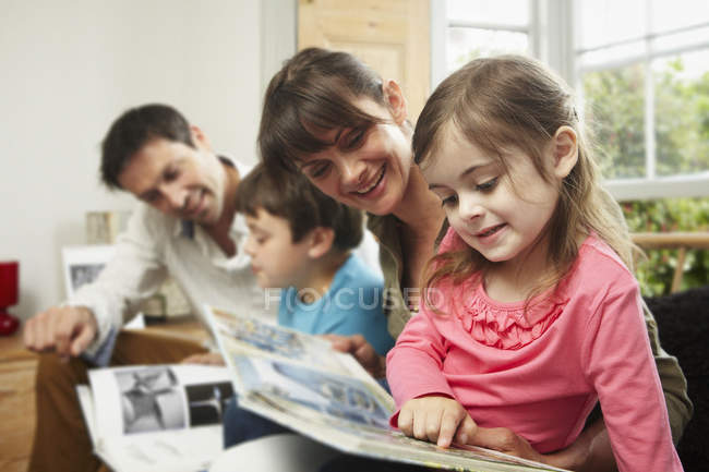 Due genitori e bambini che leggono insieme a casa . — Foto stock