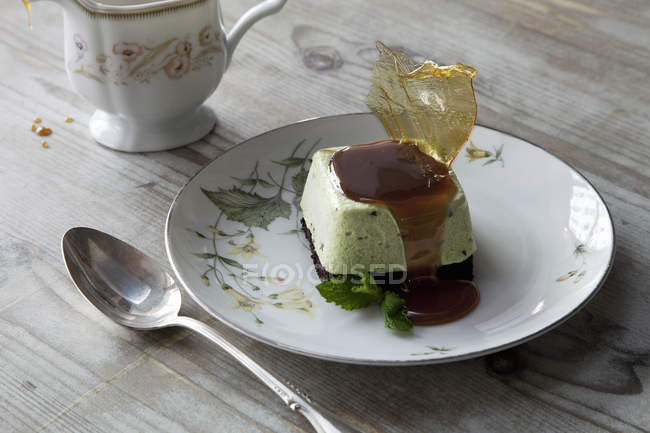 Sweet dessert dish with sugarwork and sauce on plate with spoon and cup. — Stock Photo