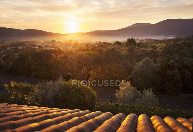 Tetto e tegole che si riflettono al tramonto con catena montuosa e villaggio nel bosco . — Foto stock