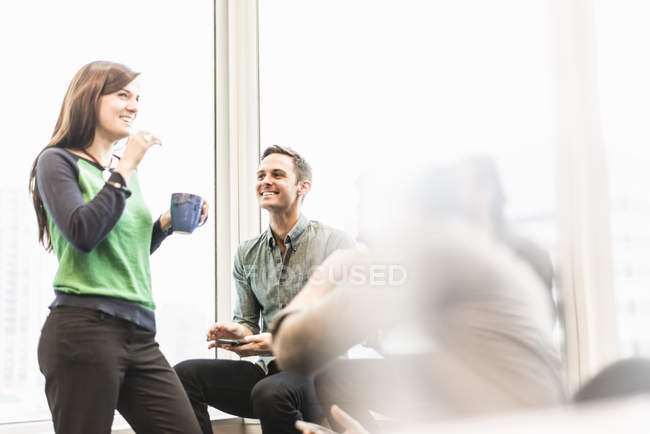 Man and woman holding cup of coffee in office with colleagues. — Stock Photo